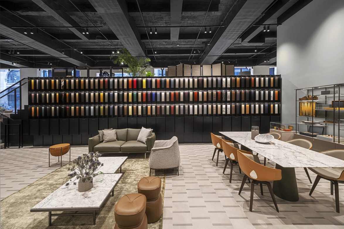 Modern showroom with sleek furniture and a wall of fabric samples; features sofas, a marble table, and leather chairs.