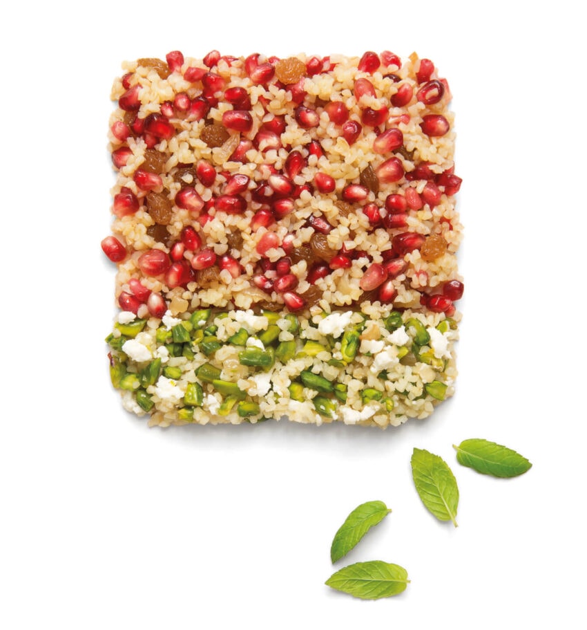 Square-shaped salad with layers of pomegranate seeds, couscous, nuts, and mint leaves garnished with fresh mint leaves.