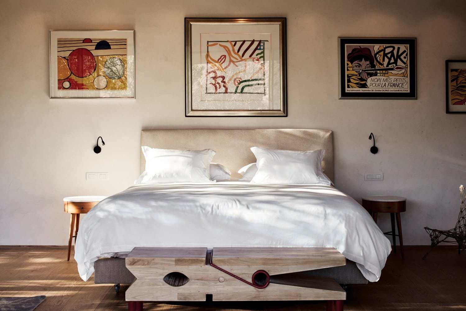 Modern bedroom with a white bed, framed abstract art on the walls, and wooden flooring.