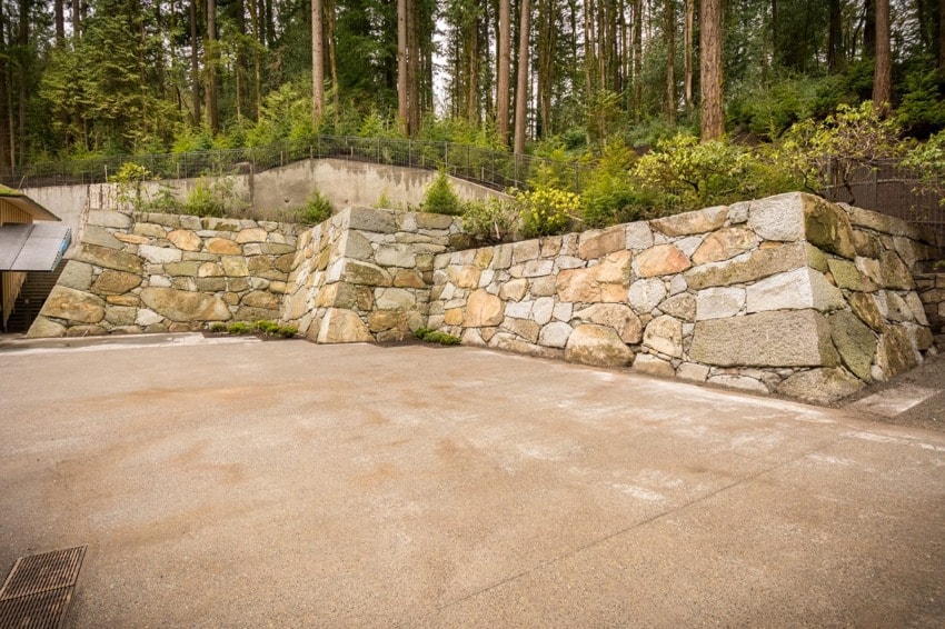 Stone retaining walls with varying rock colors surrounded by a forest of tall pine trees in the background.