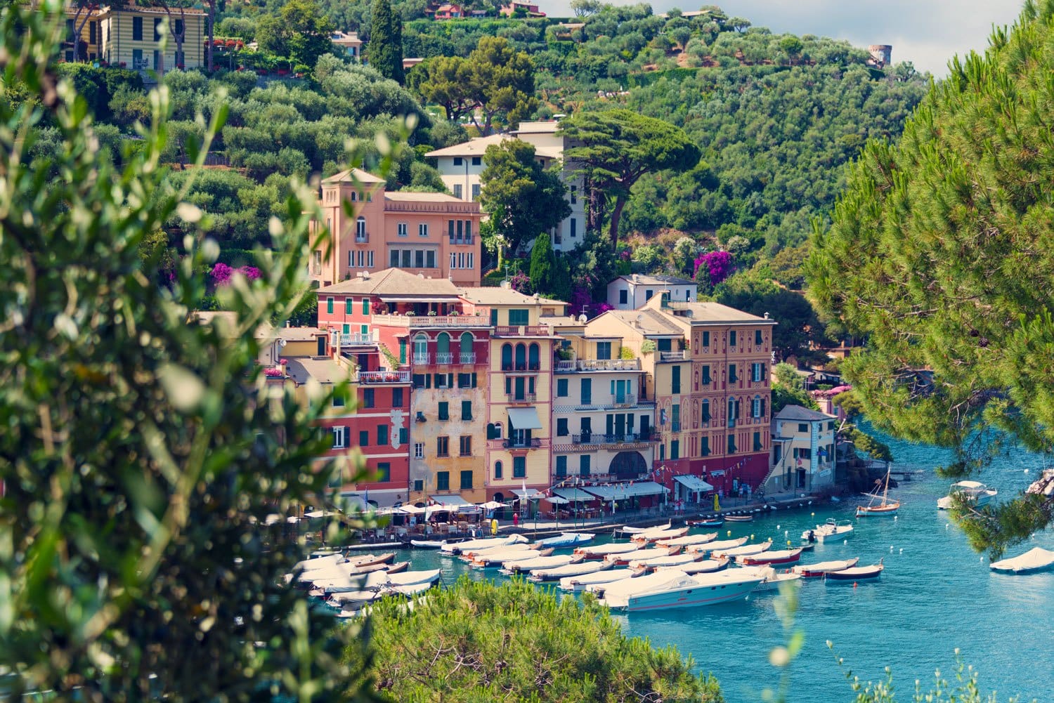 Colorful buildings and boats along the waterfront in a picturesque coastal village surrounded by lush greenery and hills.