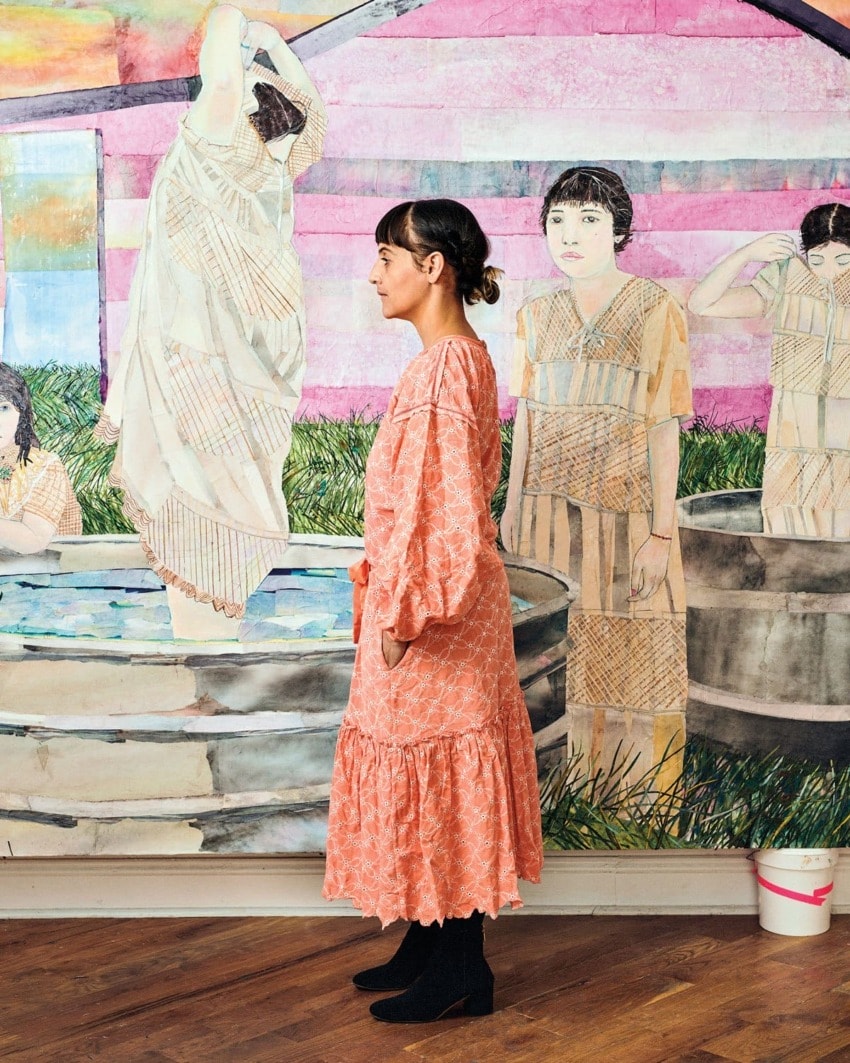 Woman in a pink dress standing in front of a colorful mural depicting figures and a water scene.