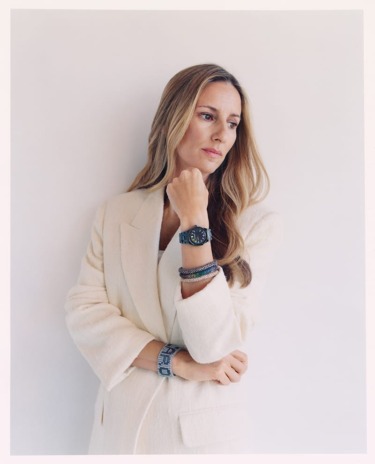 Person in a beige blazer, looking away, wearing a watch and bracelets against a white background.
