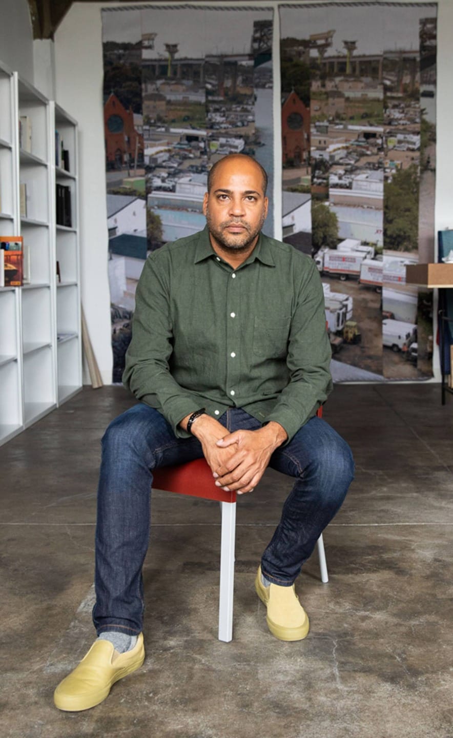 Man sitting on a chair in a modern office with bookshelves and large mural in the background.
