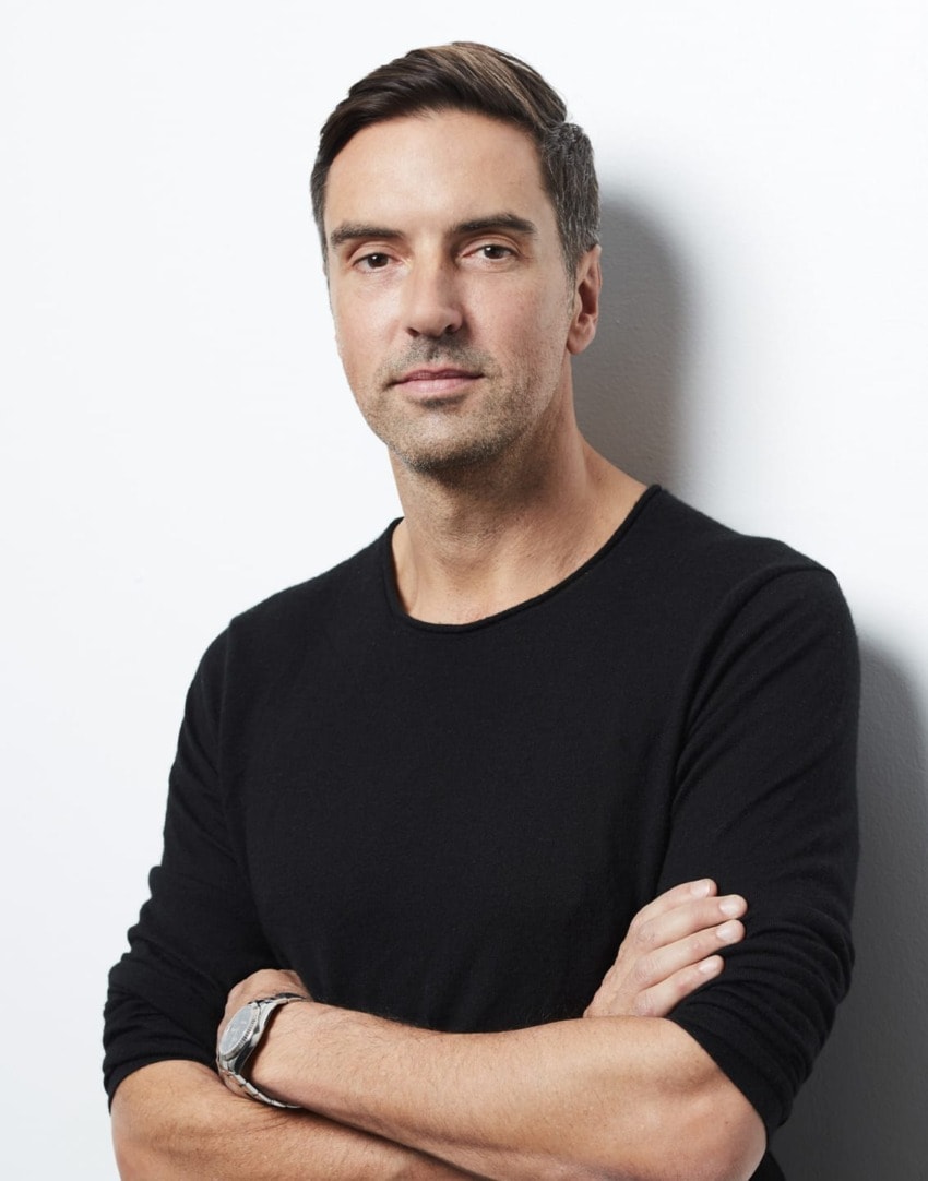 Man in black sweater with arms crossed against a white background.