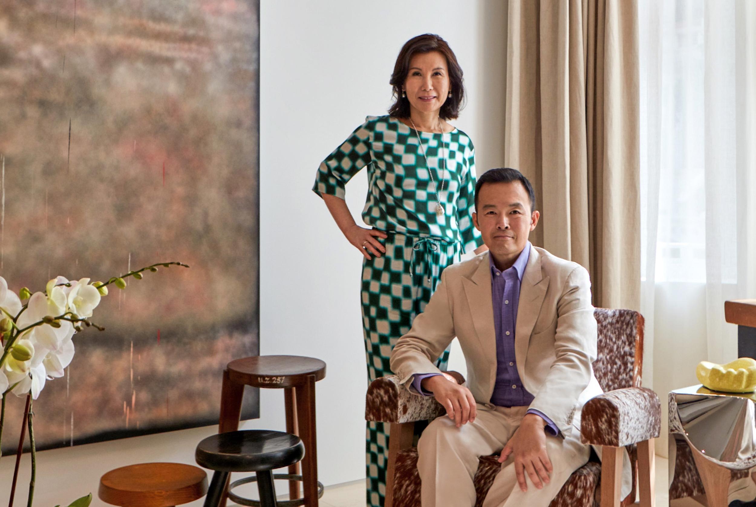 Two people, one standing and one seated, in a stylish living room with modern decor and natural light from a window.