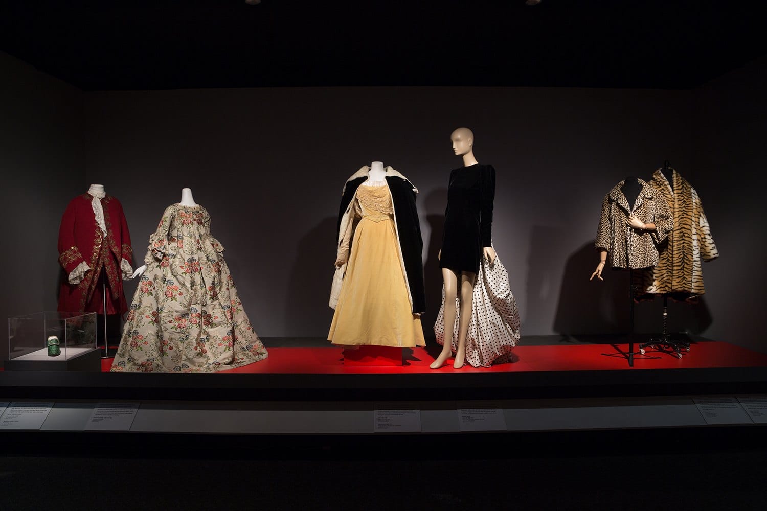 Installation view of "Power Mode: The Force of Fashion" at The Museum at FIT including 18th-century garments, an ermine cape and Carolina Herrera frock, a 1960s Dior leopard coat and more contemporary faux fur jacket by Dolce & Gabbana.
