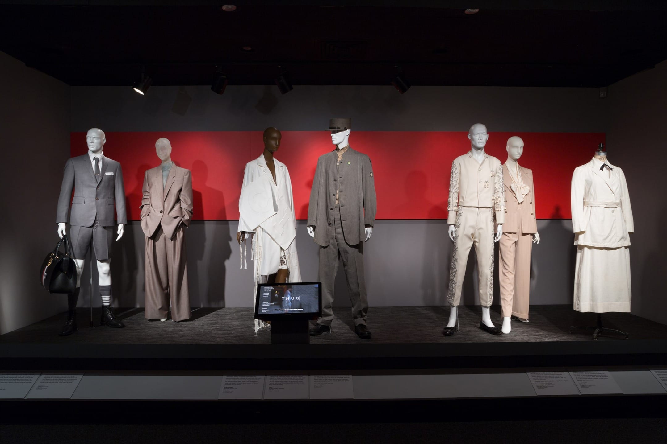 Fashion exhibit featuring seven mannequins dressed in various stylish suits and outfits under focused lighting.