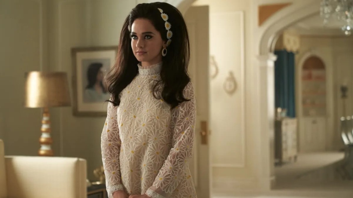 Woman in vintage floral dress with daisy headband standing in a elegantly decorated room.