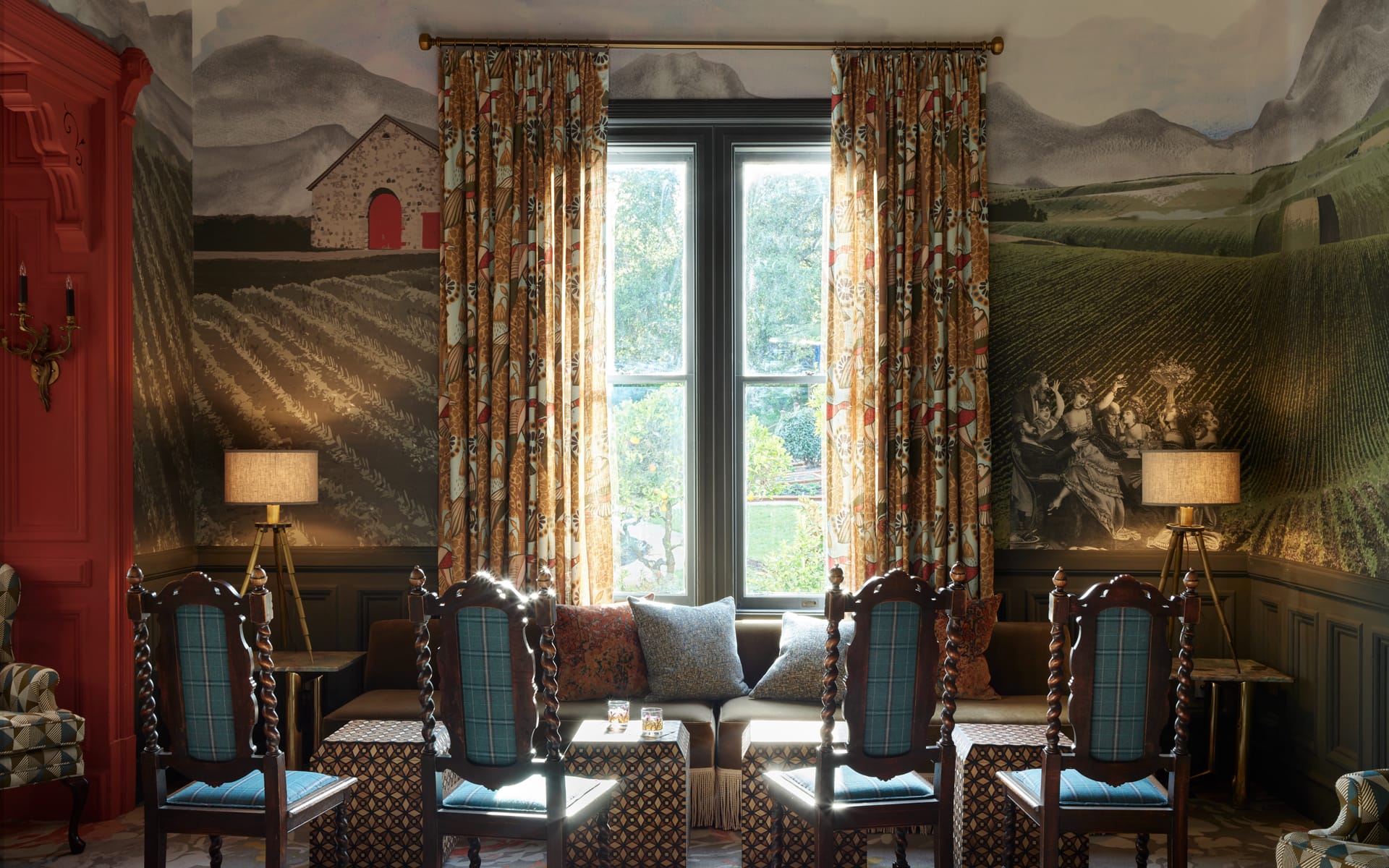 Cozy room with vintage chairs, decorative wall mural, large window with curtains, and soft lighting from table lamps.