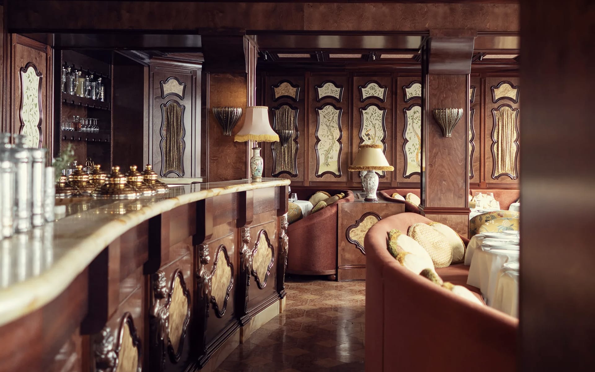 Elegant vintage-style lounge with ornate wooden panels, plush seating, marble bar, and soft ambient lighting.