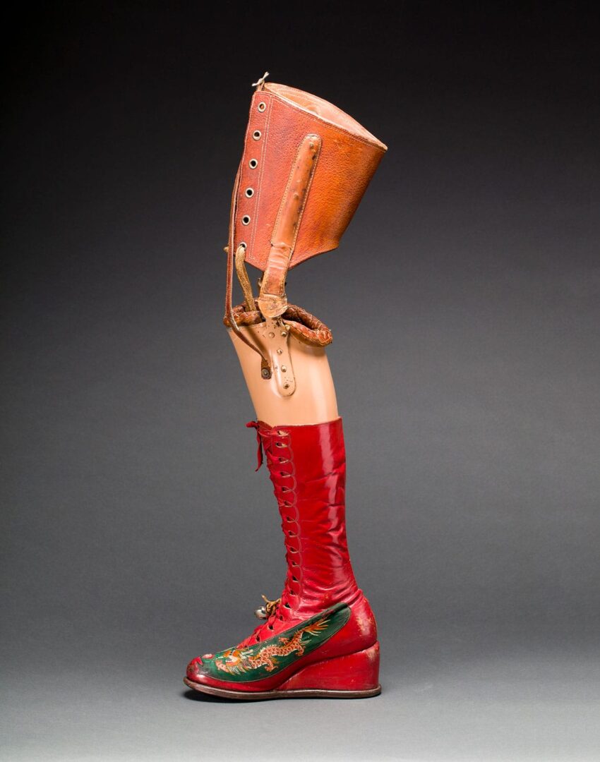 Prosthetic leg with red boot and brown leather attachment on a gray background.
