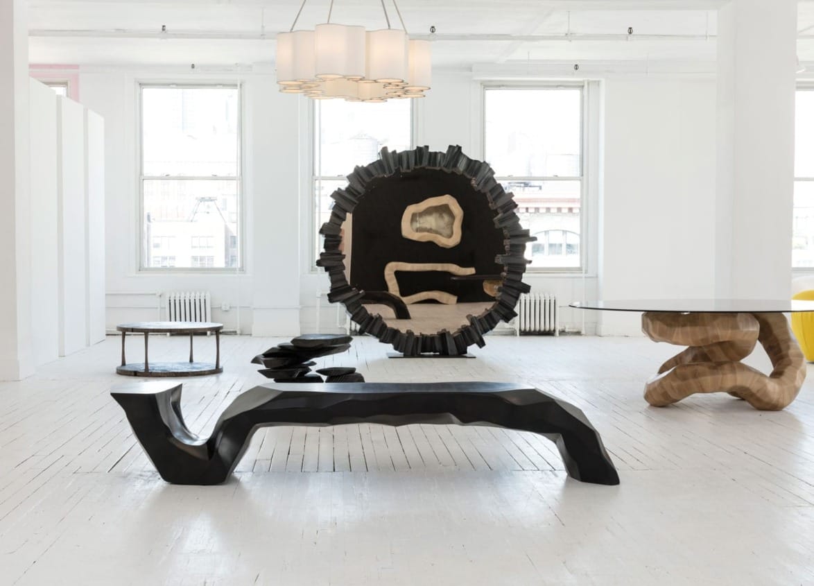 Modern art gallery with abstract wooden furniture and sculptures in a spacious, light-filled room.