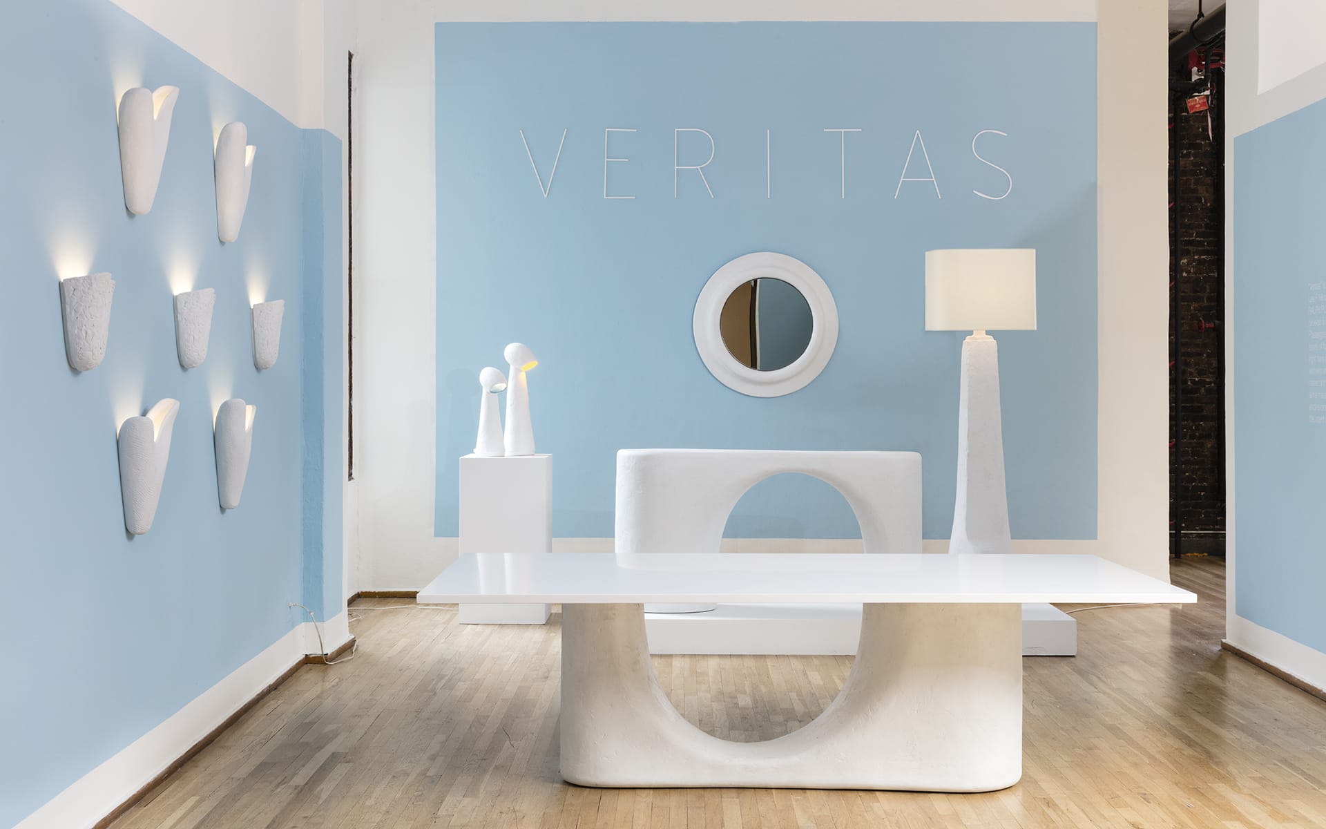 Modern showroom with blue walls, abstract white furniture, wall lights, and circular reflective art piece on display.