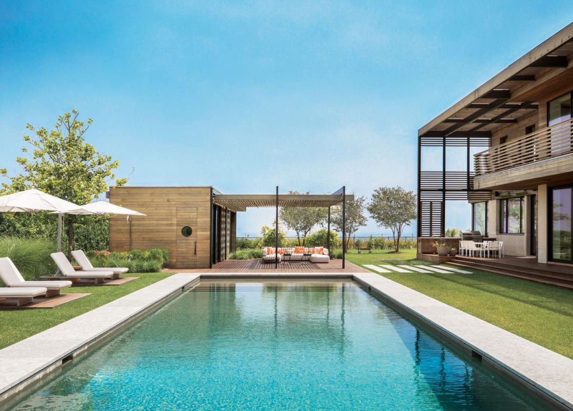 Modern backyard with a swimming pool, lounge chairs, trees, and a contemporary house on a sunny day.