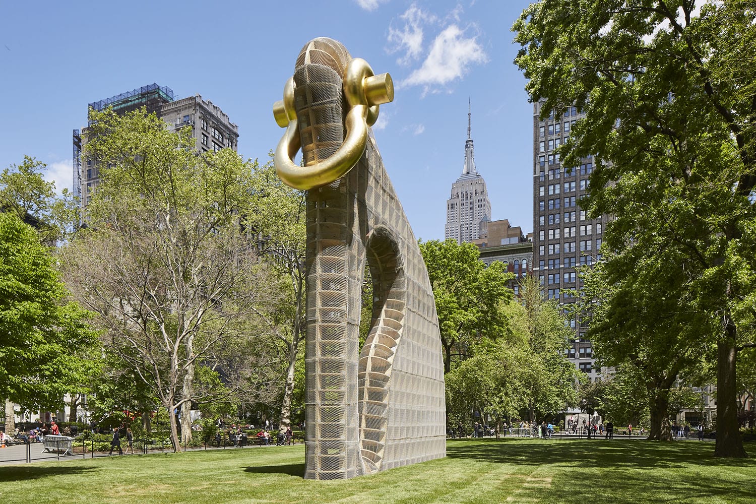 Large outdoor sculpture resembling a gold-tusked elephant in a city park with buildings and trees in the background.