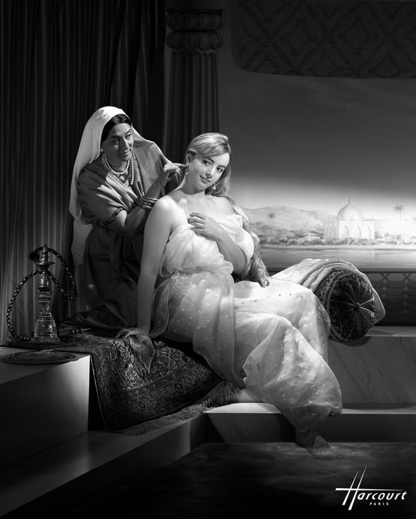 A woman in elegant attire sits while another woman adjusts her hair, with an ornate background and intricate details.