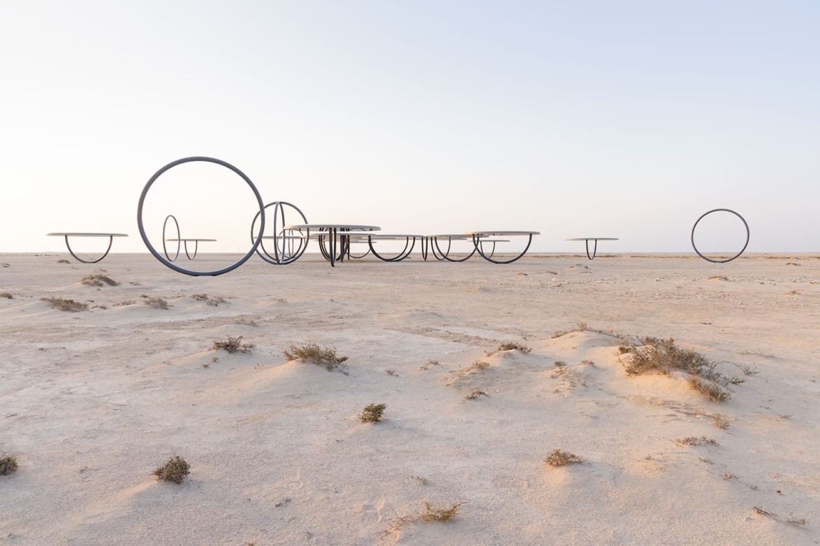 Art installation in a desert landscape with circular structures partially buried in sand, under a clear sky.