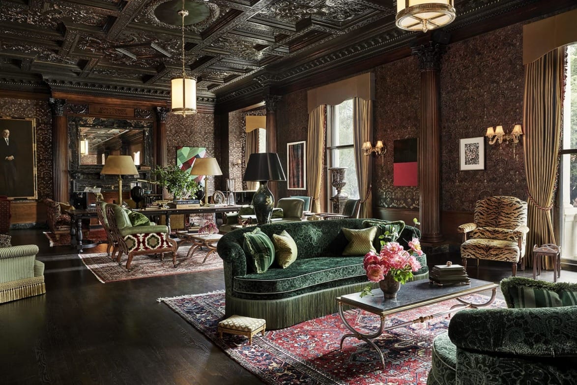 Luxurious living room with ornate dark wood ceiling, green velvet sofas, and decorative rugs.