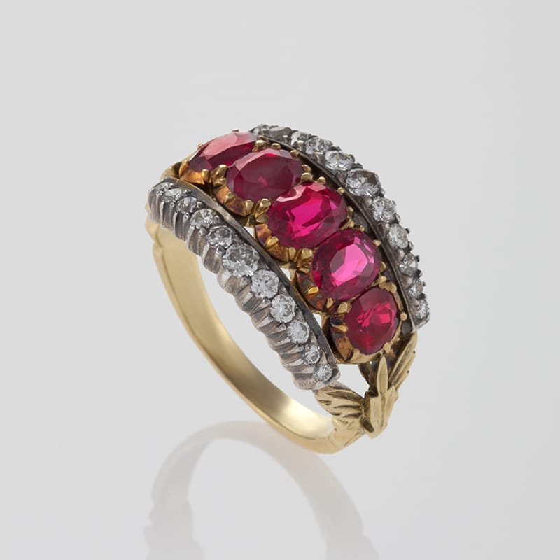 Gold ring with four red gemstones and diamond accents arranged in an ornate design.