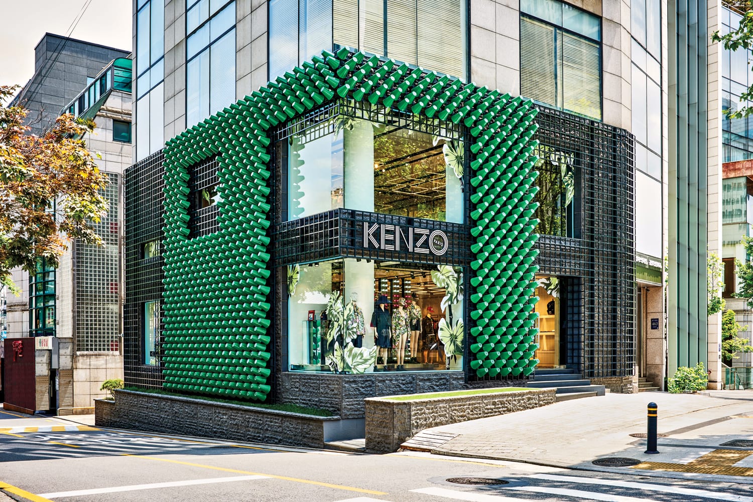 Modern urban store with distinctive green exterior and large KENZO signage on a sunny day.