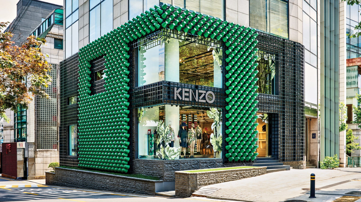 Modern Kenzo store with green geometric facade on corner of a street with large windows displaying fashion items.