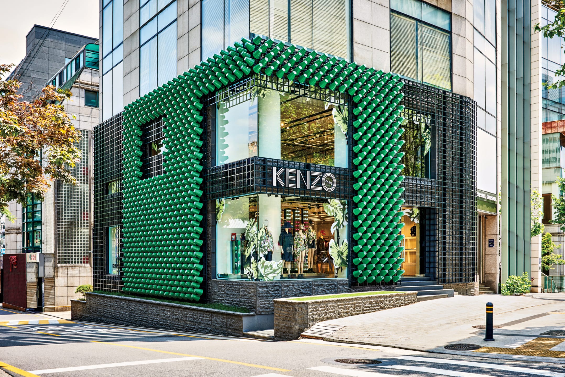 Modern Kenzo store with green geometric facade on corner of a street with large windows displaying fashion items.
