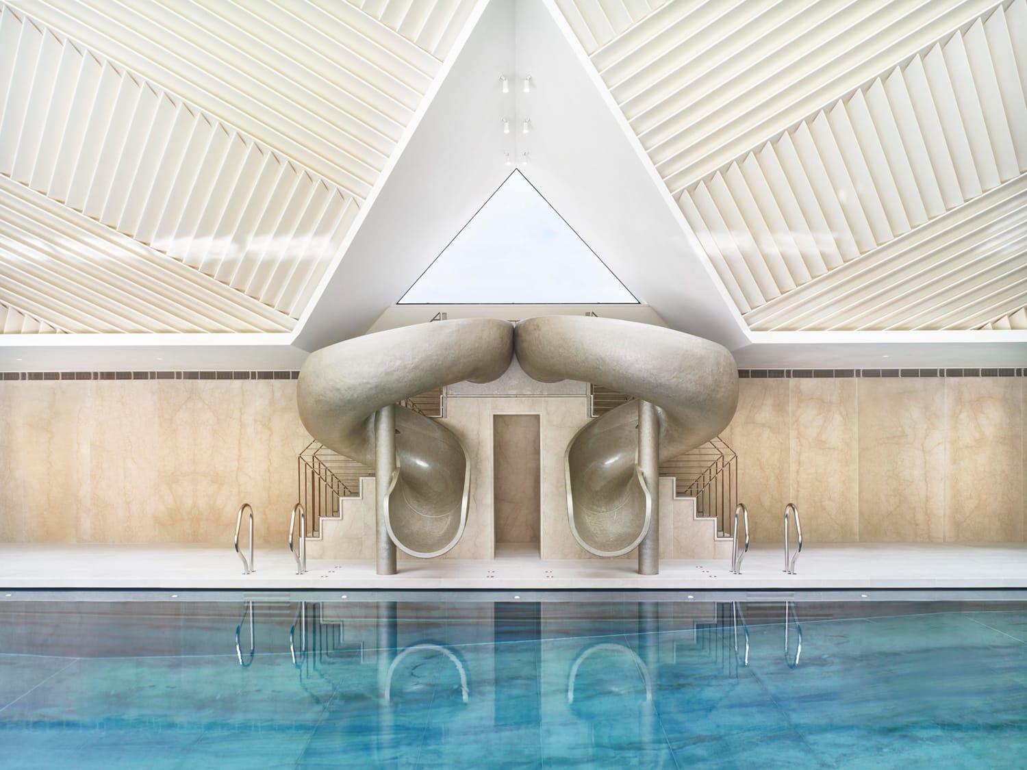 Modern indoor pool with two matching spiral slides, sleek architecture, and a reflective water surface.