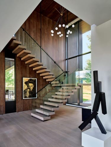 Modern interior with floating staircase, wooden walls, large window, contemporary art piece, and geometric sculpture.