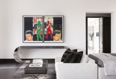 Modern living room with white couch, decorative pillows, abstract art on the wall, and a sleek console table.