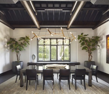 Modern dining room with dark wooden table, black chairs, large window, geometric chandelier, and potted plants.