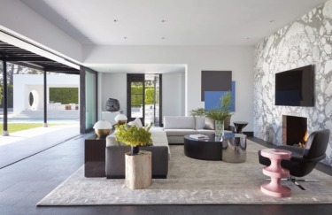 Modern living room with gray sofa, marble fireplace, and large windows open to a pool and patio area.