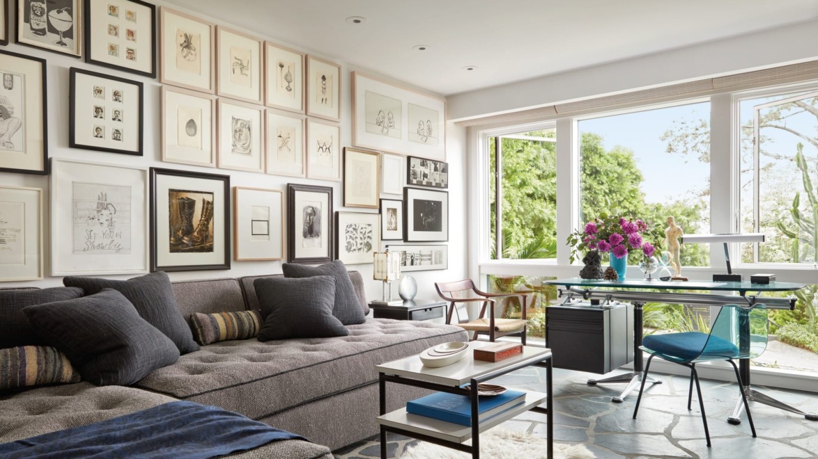 Modern living room with a gray sofa, wall art, a glass desk, and a large window with garden view.