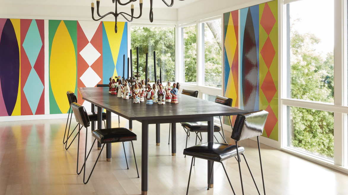 Dining room with a large table, modern black chairs, and vibrant geometric pattern wallpaper on the walls.