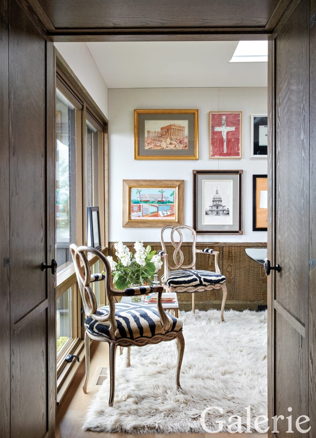 Chic sitting area with elegant chairs, plush rug, and framed art on walls, viewed through a wooden doorway.
