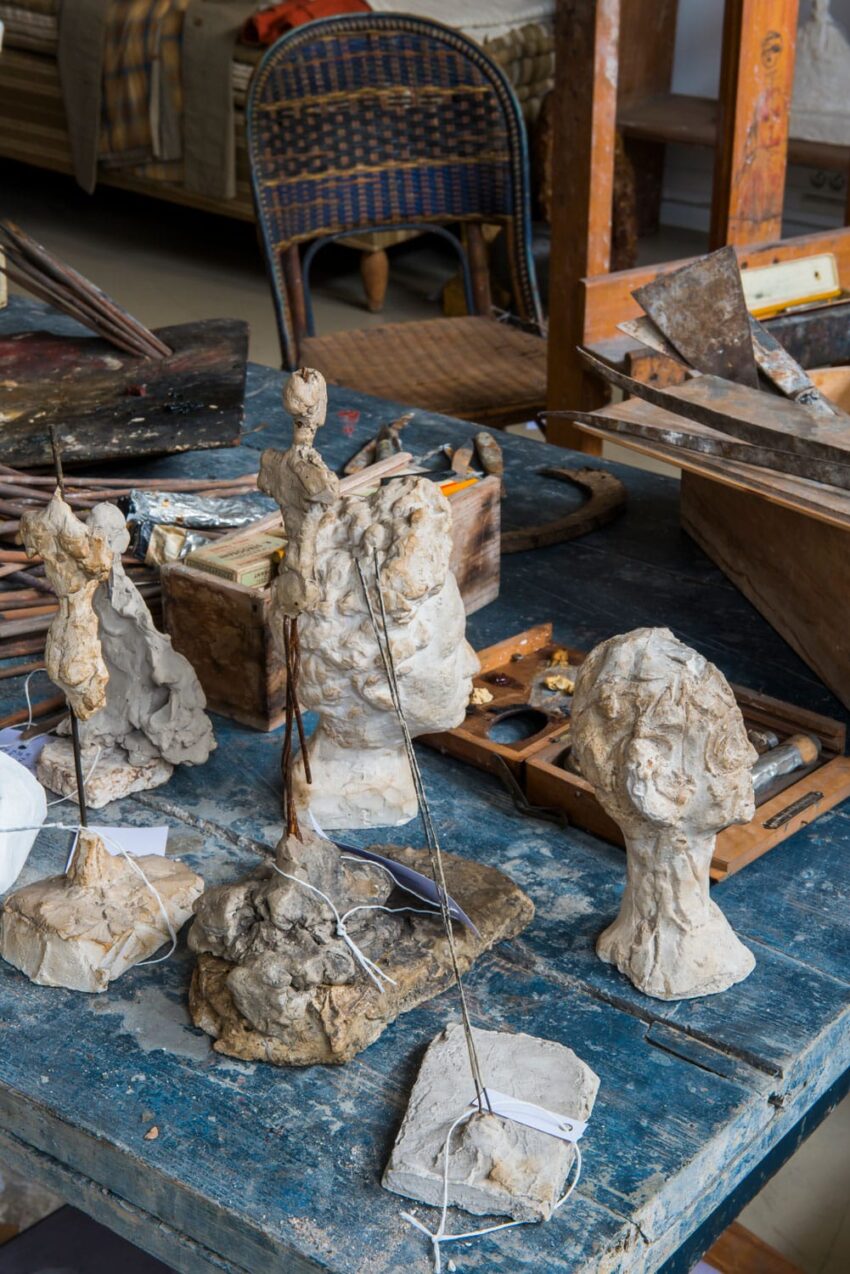 sculpture models on a blue wooden table in an artist's studio with various tools and materials in the background