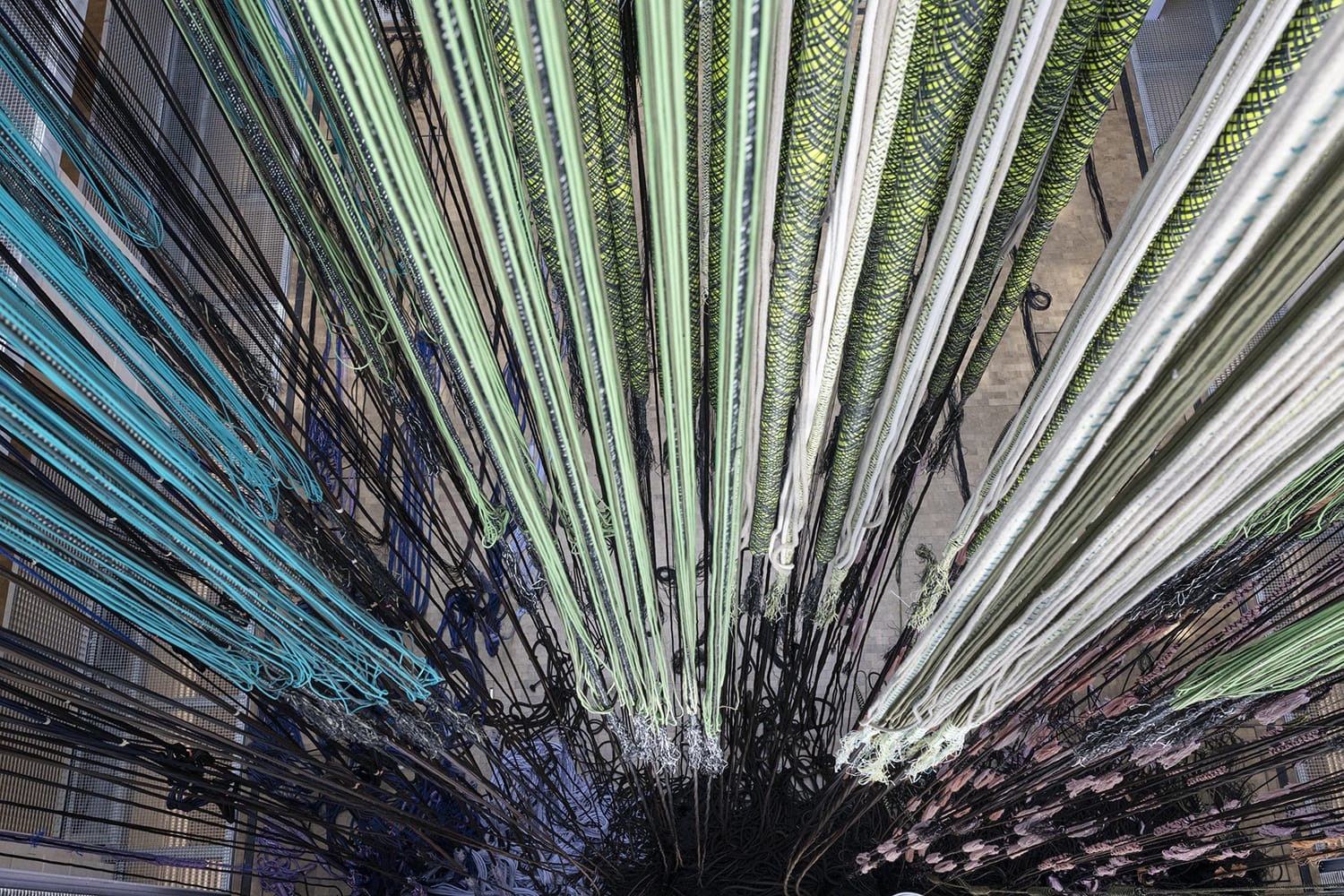 Strings of multicolored yarn hung vertically, creating a visually striking pattern from a top-down perspective.