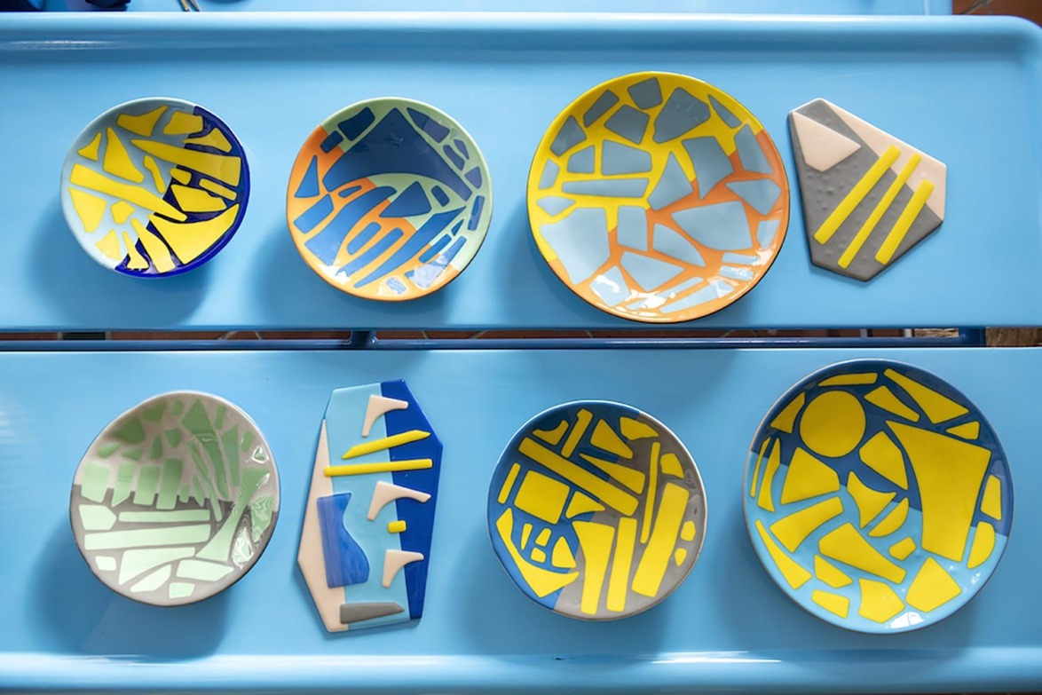 Colorful ceramic plates with abstract mosaic designs displayed on a bright blue surface.