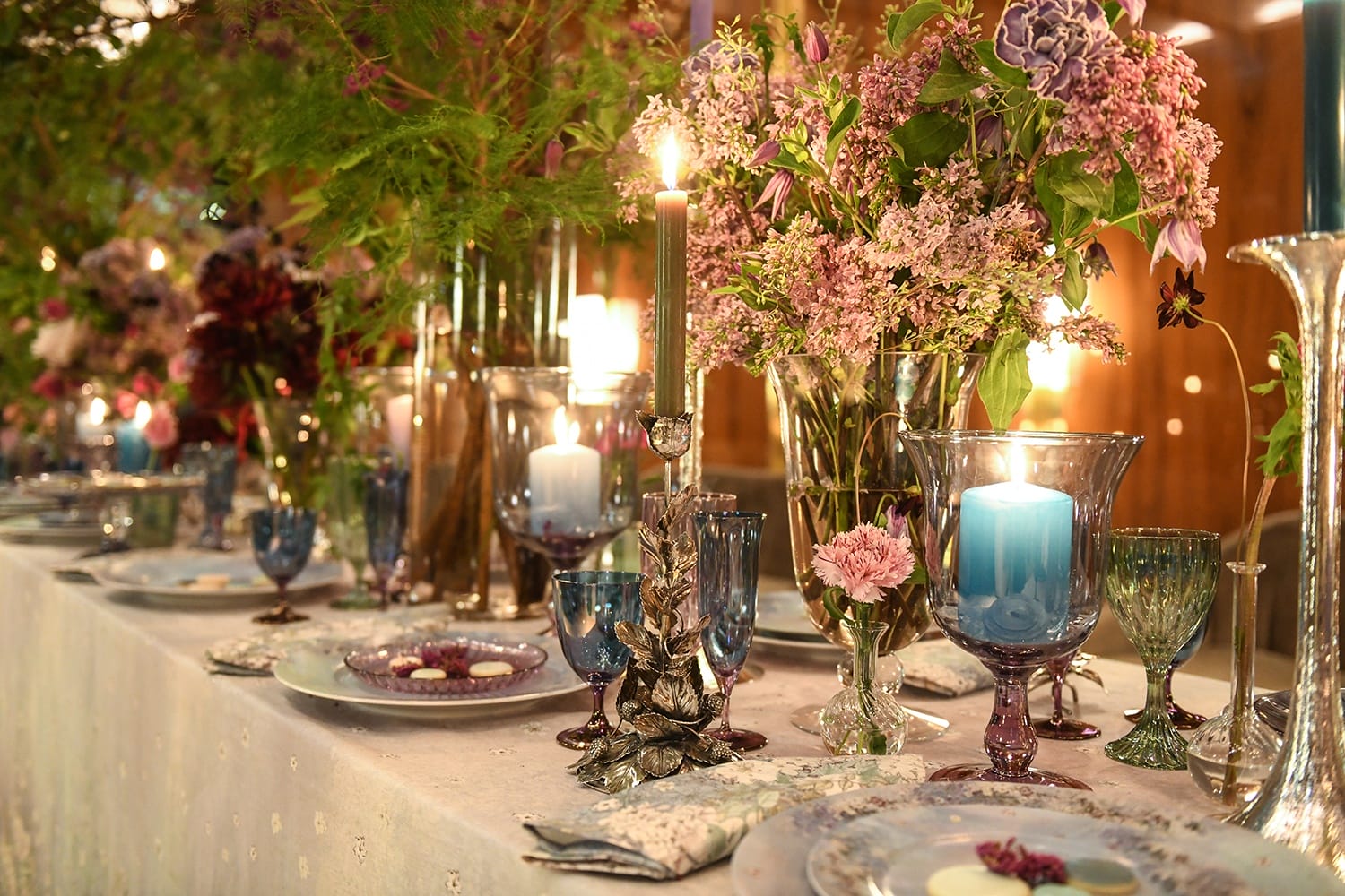 Elegant dining table setup with floral centerpieces, candles, and vintage glassware in a warm, inviting atmosphere.