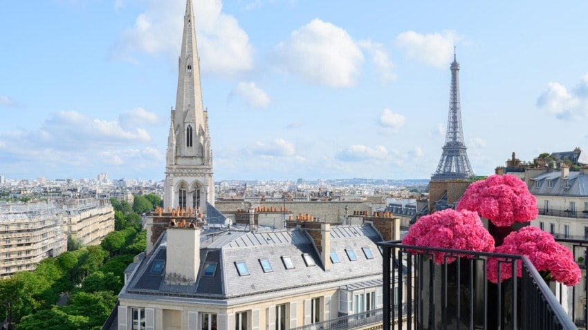 Paris rooftops with Eiffel Tower in the background and a balcony adorned with vibrant pink flowers on a sunny day.