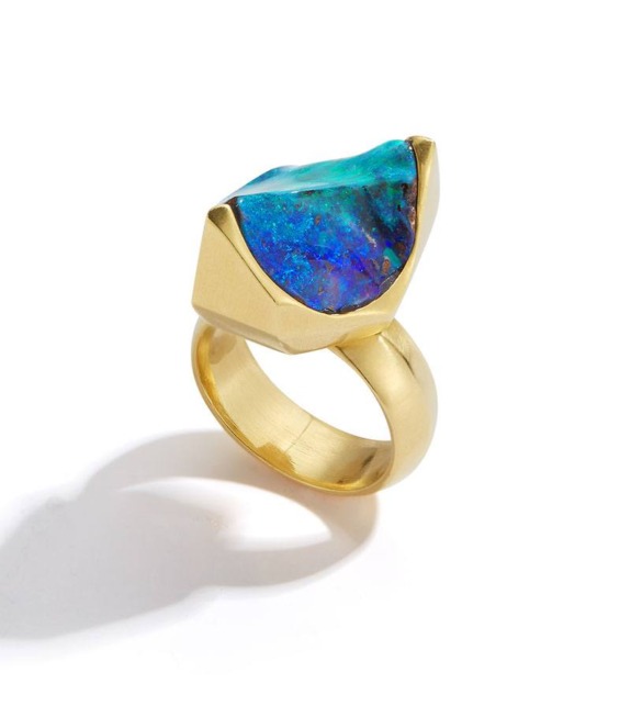 Gold ring featuring a large, raw blue opal gemstone on a white background.