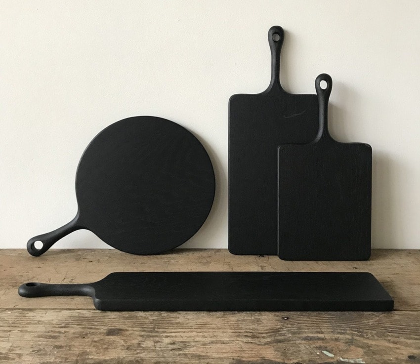 Set of four black cutting boards in various shapes and sizes displayed against a plain wall on a wooden surface.