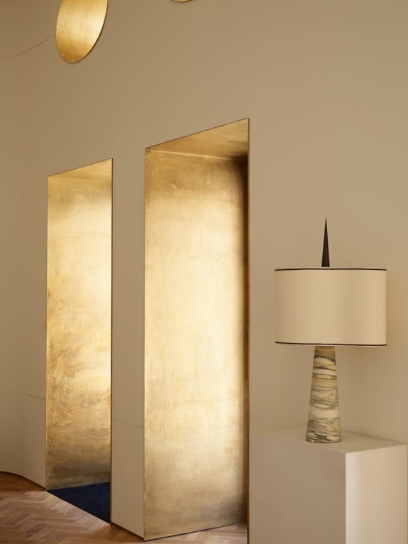 Elegant interior with two gold-framed mirrors, a modern lamp on a white pedestal, and wooden flooring.