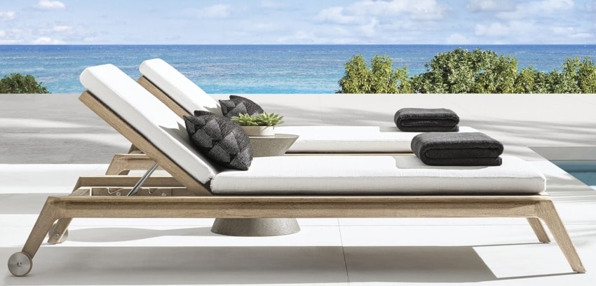 Two wooden lounge chairs with cushions and towels overlooking the ocean and a clear blue sky.