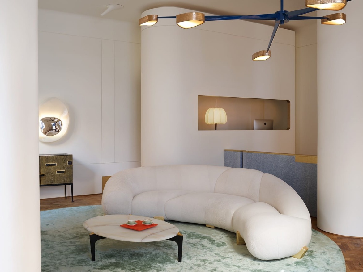Modern living room with a curved sofa, oval table, blue chandelier, and wall-mounted mirror above a low cabinet.