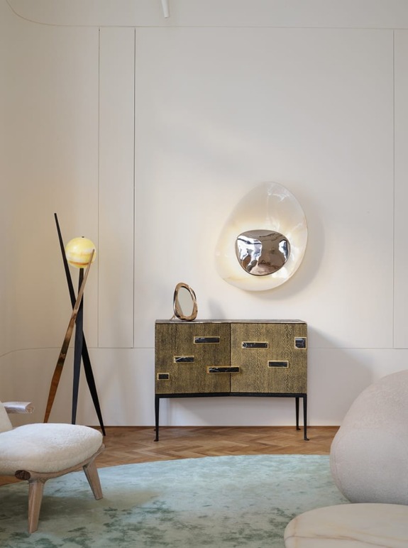 Modern living room with stylish cabinet, abstract wall art, unique floor lamp, and plush chairs on a soft green rug.