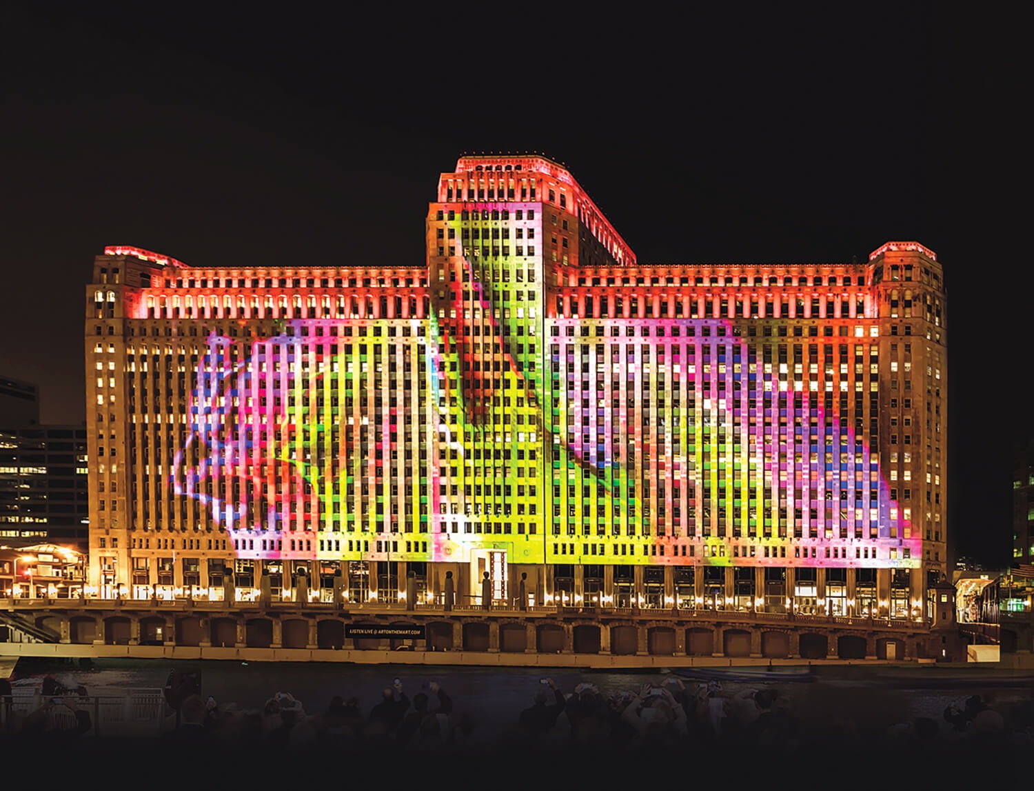 Colorful light projection on a large, historic building at night, with vibrant abstract patterns illuminating the facade.