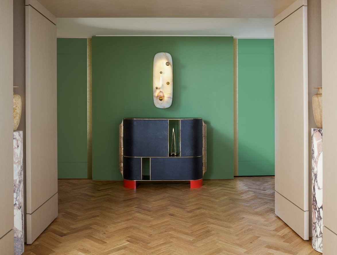 Modern hallway with a green accent wall, unique wall-mounted light fixture, and a stylish console table on herringbone wood floor.