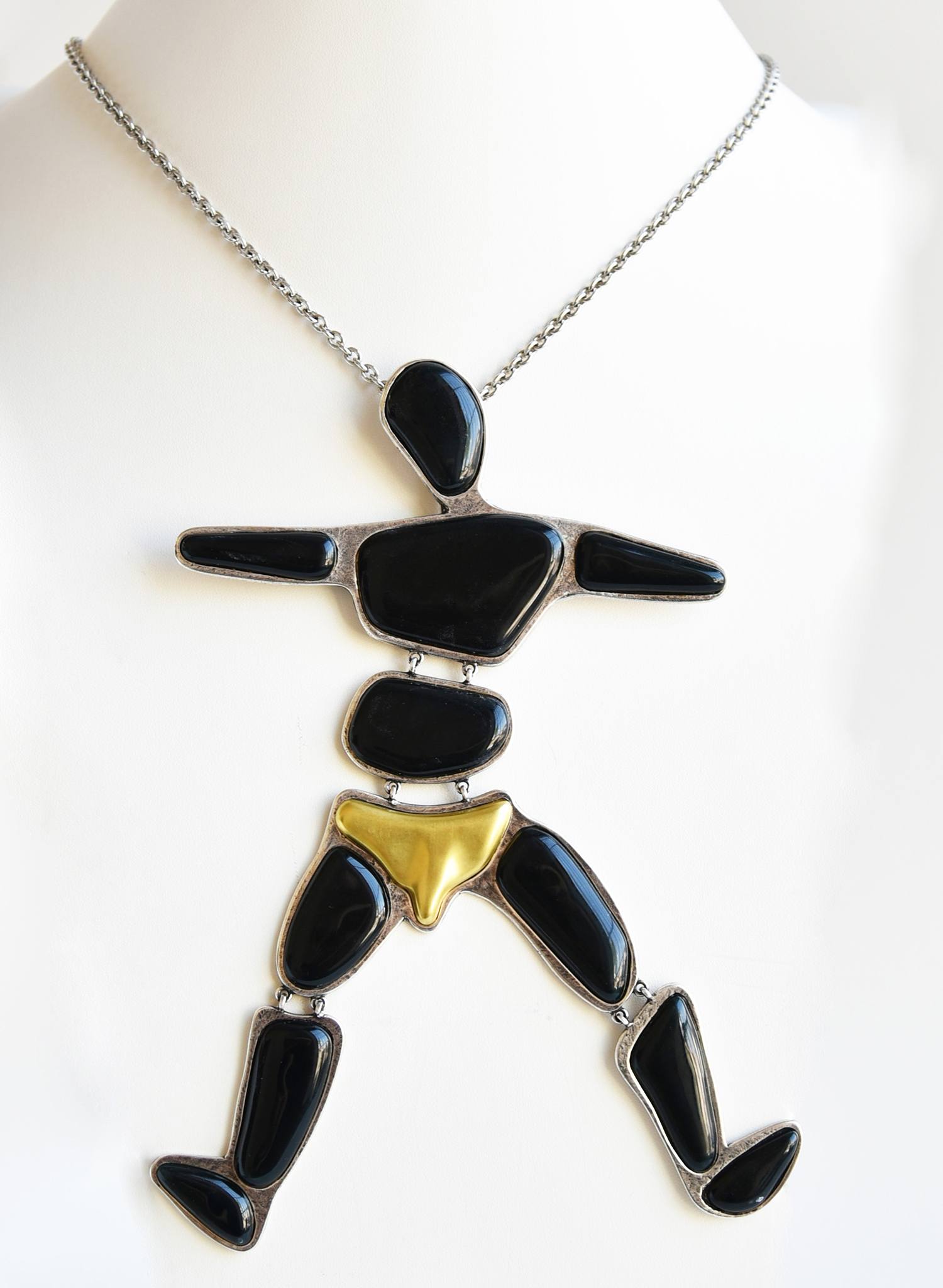 Unique necklace featuring an abstract human figure made of black stones and a gold-tone element, on a white background.