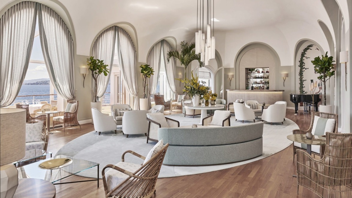Luxurious hotel lounge with elegant furniture, large windows, ocean view, and modern decor elements including plants and lighting.